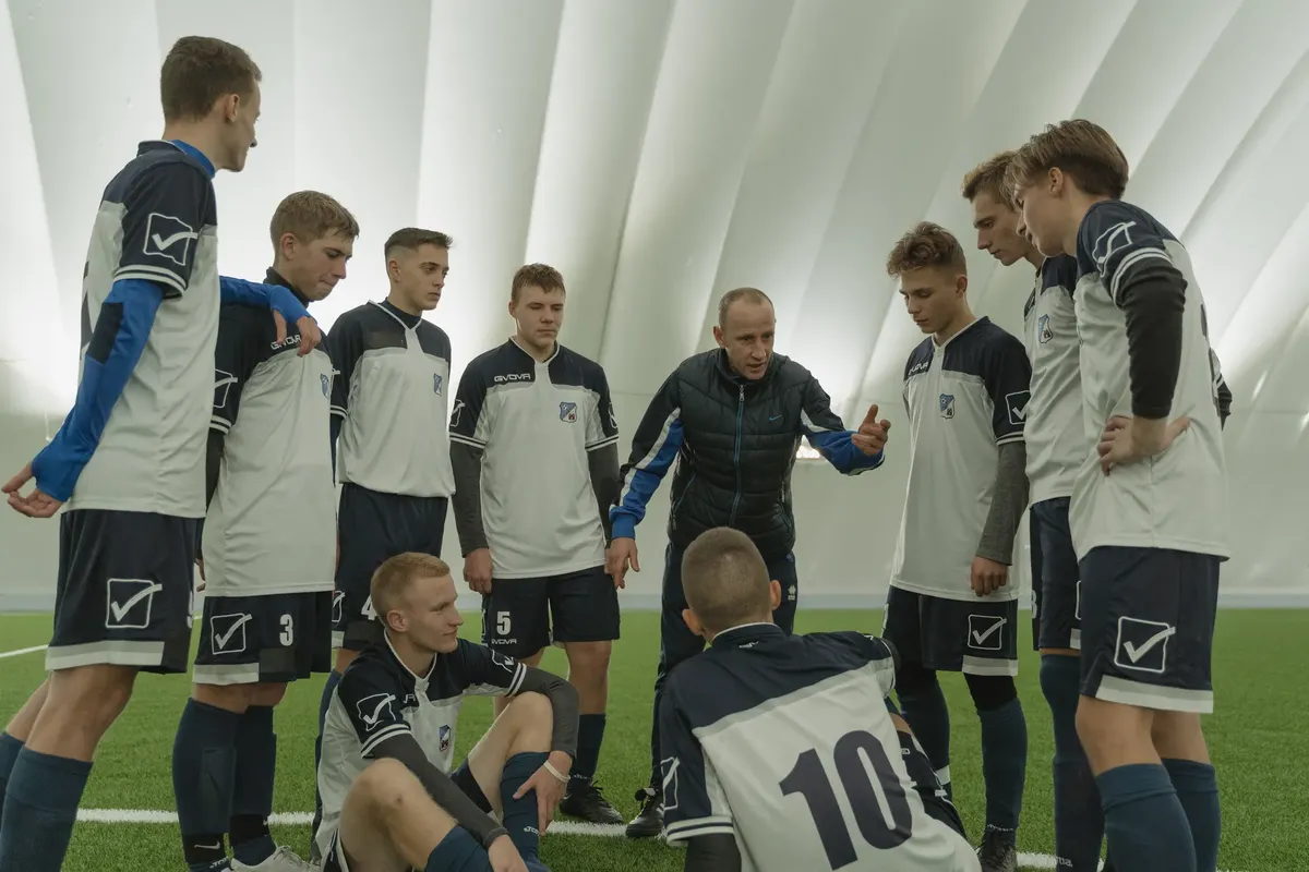 Coach giving a pep talk to a men's soccer team indoors.