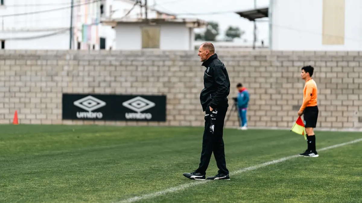 A soccer coach attentively observes a training session, standing by the sideline.