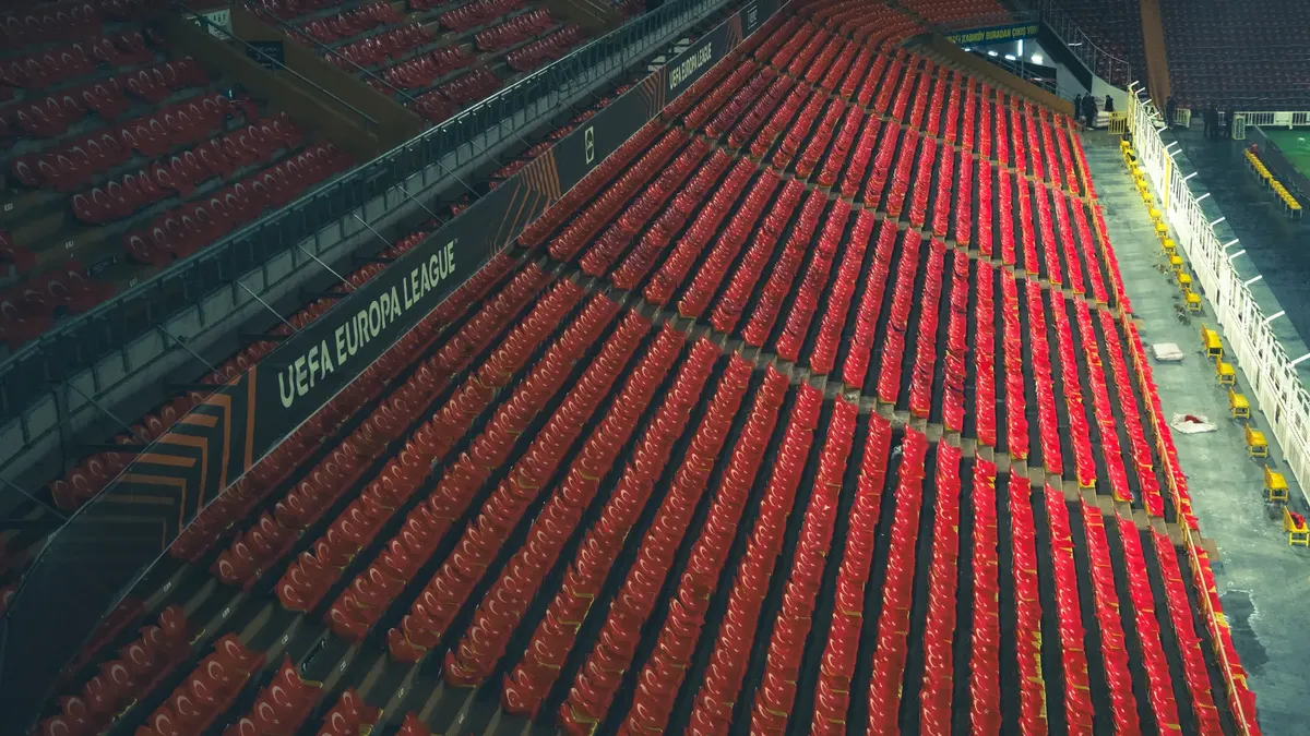 Rows of empty red seats in a UEFA Europa League stadium, captured from above.